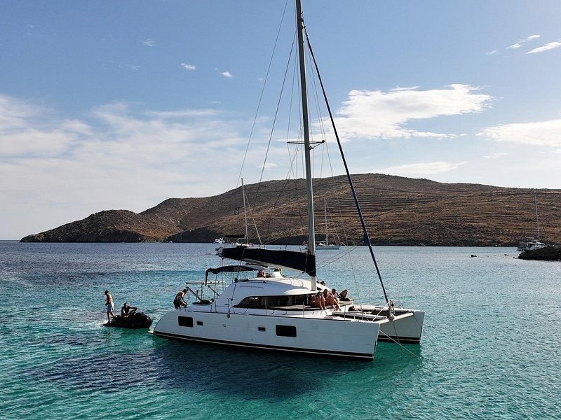 A catamaran lying at anchor in a sheltered bay under a bare headland