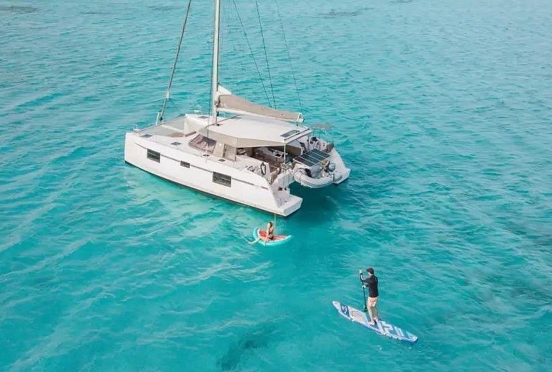 A paddleboard alongside a catamaran anchored in shallow turquoise water