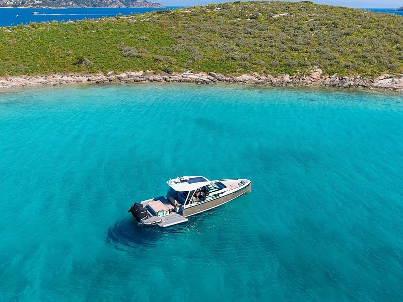 A boat anchored over pale sand in the turquoise shallows off an uninhabited island